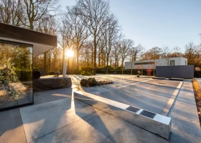 alice-et-paul-besoins Maison moderne avec terrasse en béton, arbres dénudés et soleil couchant à l'arrière-plan, reflet d'un sapin décoré dans une vitre.