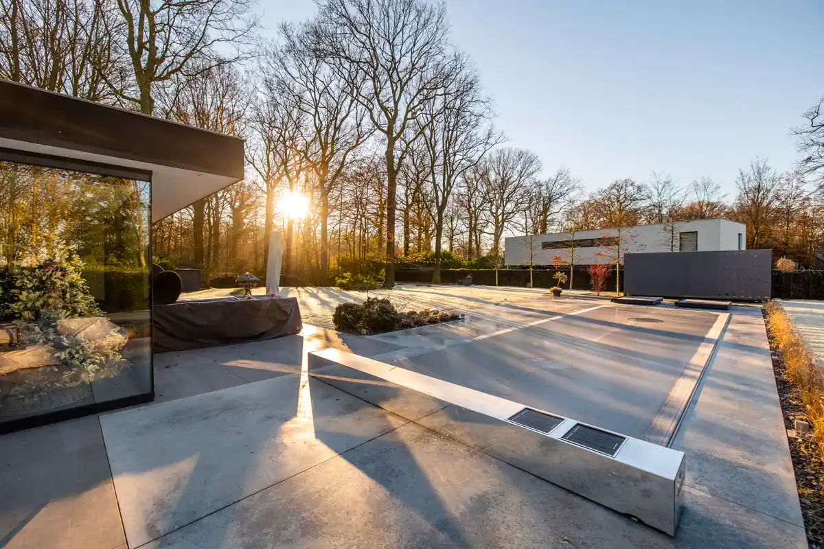 Maison moderne avec terrasse en béton, arbres dénudés et soleil couchant à l'arrière-plan, reflet d'un sapin décoré dans une vitre.