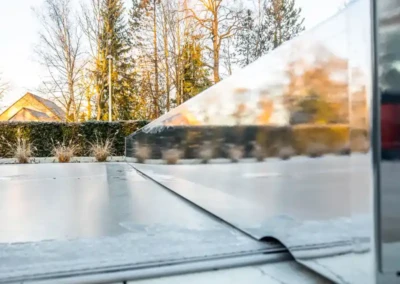 alice-et-paul-gallery-04 Surface de piscine couverte avec une structure métallique réfléchissante, entourée de végétation et d'arbres en arrière-plan sous un ciel dégagé.