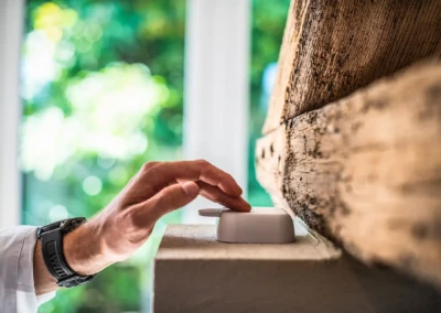 Main appuyant sur un interrupteur blanc monté sur un mur en bois, avec une fenêtre floue en arrière-plan.