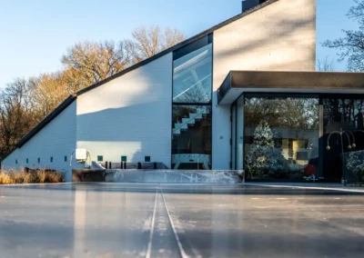 lhiver-chez-alice-et-paul Maison moderne avec façade blanche et grandes fenêtres, entourée d'arbres dénudés, et terrasse en béton au premier plan.