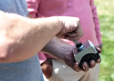 linstallation-chez-juliette-leon-5 Deux personnes manipulant un boîtier métallique avec une clé, une portant un t-shirt gris et l'autre un polo rose, en extérieur.