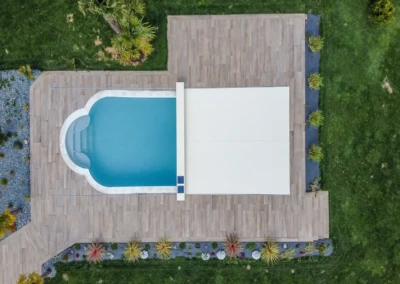 Chez-Charlotte-et-Pierre-2 Vue aérienne d'une piscine rectangulaire avec couverture blanche, entourée de terrasse en bois et de pelouse verte.