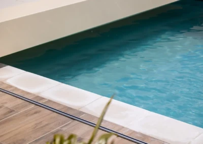 Chez-Charlotte-et-Pierre-4 Une piscine aux eaux bleues est bordée de dalles blanches et d'un sol en bois clair.