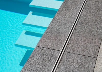 Chez-Elena-et-Nathan-6 Des dalles grises en pierre entourent une piscine d'eau bleue avec des marches immergées.