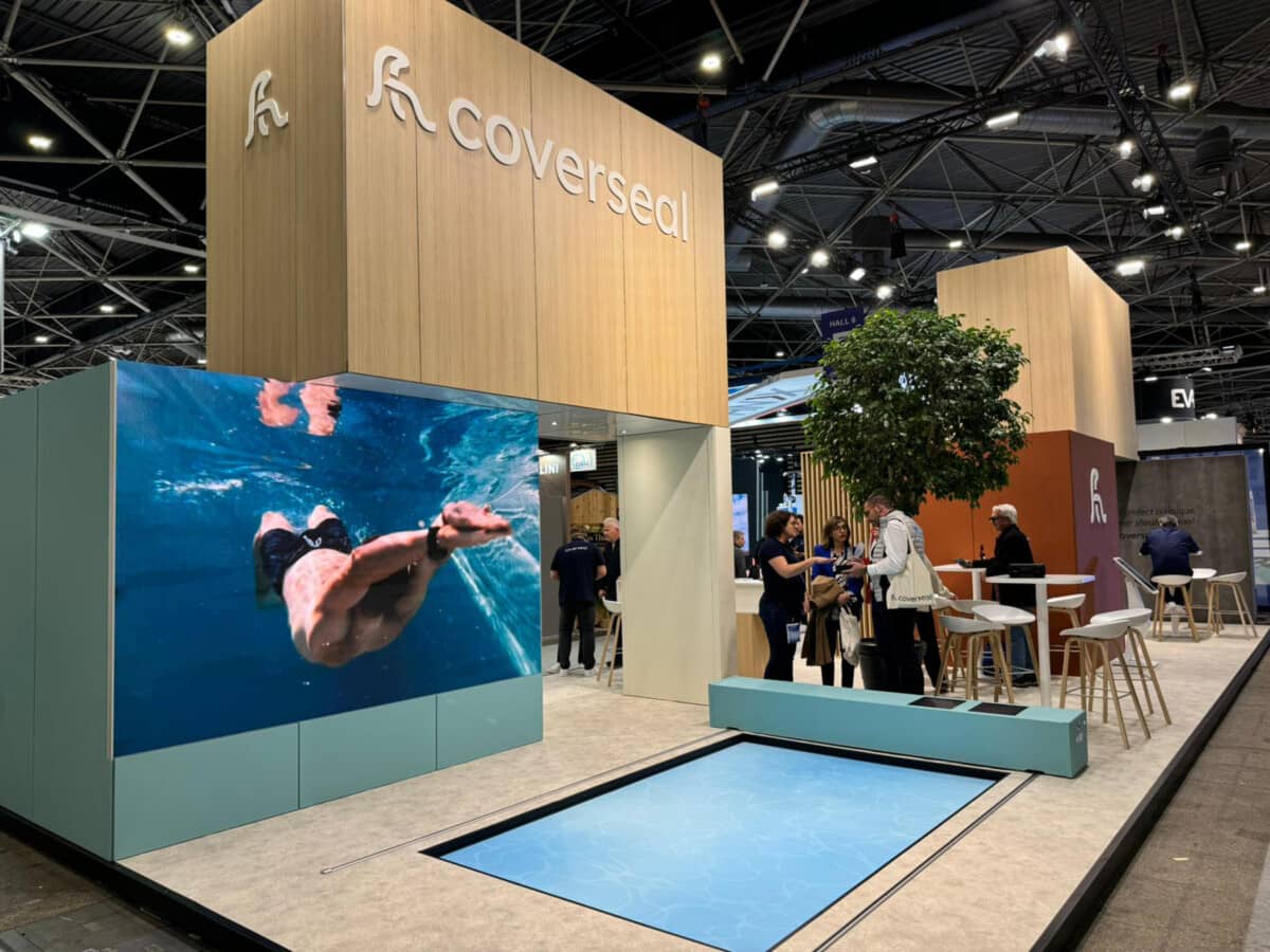 Stand Coverseal avec un grand écran affichant un nageur sous l'eau, entouré de visiteurs et de mobilier moderne sous un plafond industriel.