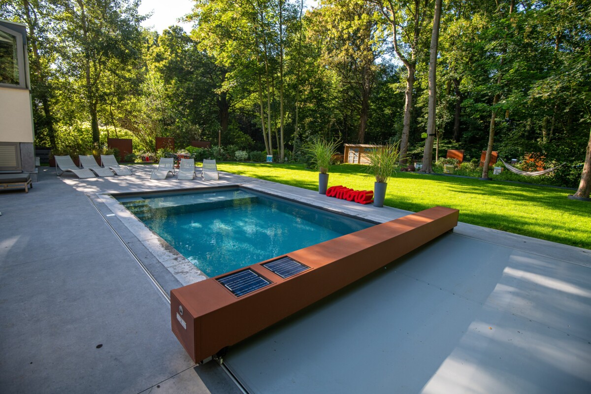 Piscine rectangulaire entourée de chaises longues blanches, bordée par une terrasse en béton et une pelouse verte avec des arbres en arrière-plan.