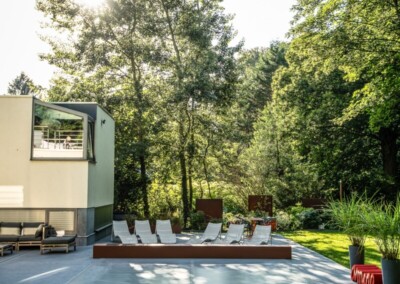 Terrasse moderne avec transats blancs alignés, entourée de verdure et d'arbres, sous un ciel ensoleillé.
