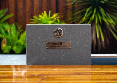 Tropical_rain32-min Panneau gris avec logo et texte "couverseal" sous la pluie, entouré de végétation verte et bordure en bois mouillé.