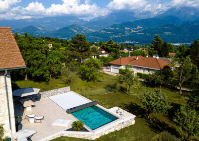 Vue aérienne d’une piscine moderne équipée d’une couverture Coverseal, intégrée à une terrasse en pierre, avec en arrière-plan les montagnes alpines.