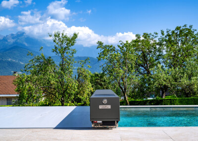 Couverture Coverseal fermée sur une piscine, avec boîtier de mécanisme gris et vue panoramique sur les montagnes et la verdure environnante.