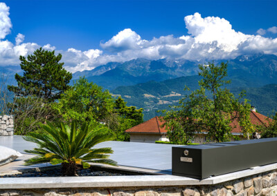 Piscine équipée d’une couverture Coverseal grise, bordée d’un jardin et surplombée par les massifs montagneux sous un ciel bleu.