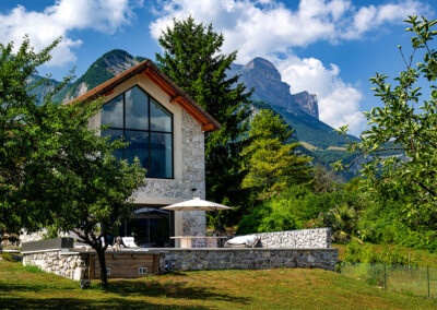 Maison en pierre de style chalet alpin avec grande baie vitrée donnant sur une terrasse et une piscine protégée par une couverture Coverseal.