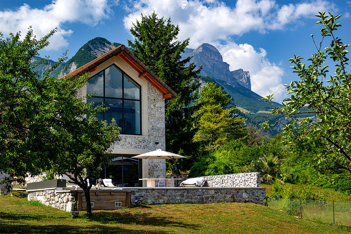 Maison en pierre de style chalet alpin avec grande baie vitrée donnant sur une terrasse et une piscine protégée par une couverture Coverseal.