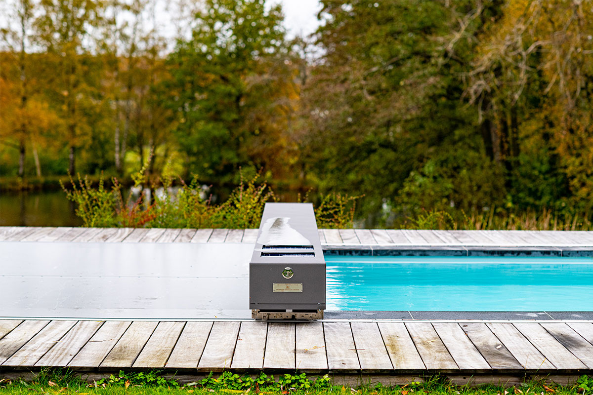 Piscine avec couverture Coverseal partiellement ouverte laissant apparaître une eau turquoise, dans un cadre naturel boisé.