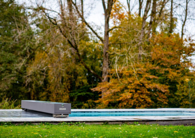 Pond3 Piscine design équipée d’une couverture Coverseal, intégrée dans une terrasse en bois au cœur d’un grand jardin arboré.