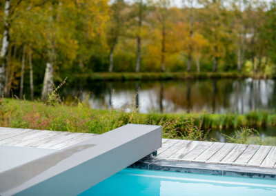 Pond4 Détail du mécanisme Coverseal au bord d’une piscine, avec vue sur un étang naturel et une végétation automnale.